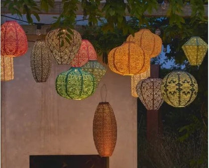 flere solcellelanterner i coral farge hengt i hage med varmt stemningslys