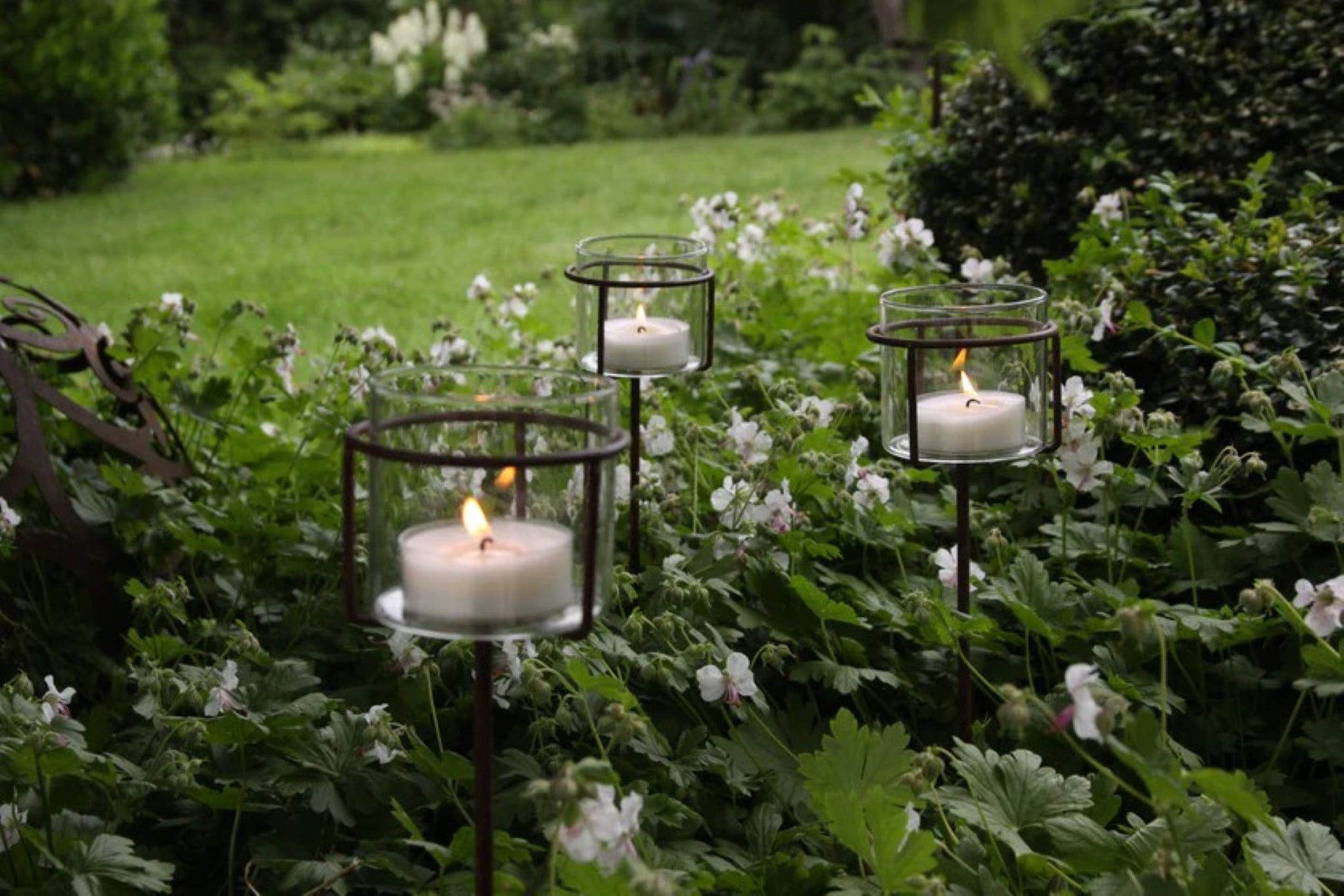 Lav telysholder med glass plassert i blomsterbed i hagen